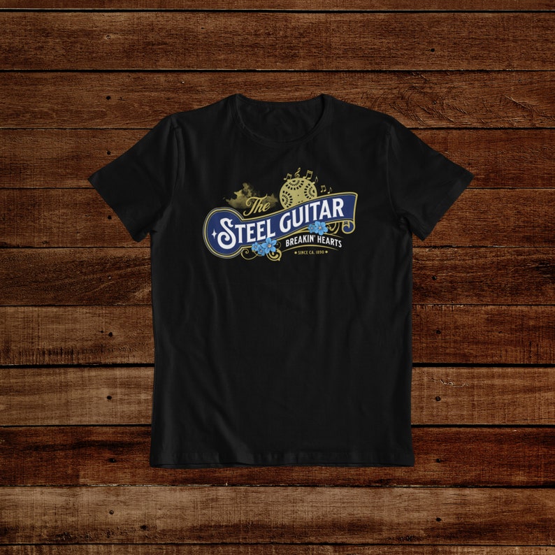 A balck t-shirt on a dark wooden background. The t-shirt has a vintage design (like 1800's soap advertisement) that says "Steel Guitar, breakin' hearts since 1890s"