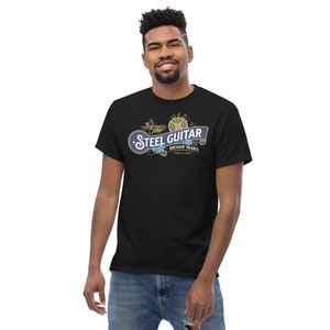 A 30-something, tall, smiling black male wearing a black t-shirt. The t-shirt has a vintage design (like 1800's soap advertisement) that says "Steel Guitar, breakin' hearts since 1890s"