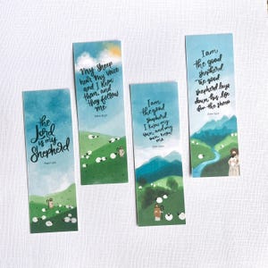 May include: Four rectangular paper bookmarks featuring watercolor-style illustrations of green hills, blue skies, and sheep. Each bookmark displays black cursive text with biblical verses including The Lord is my Shepherd and John 10:27, 10:14, 10:11.