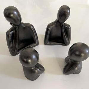 En familj av drömska tänkare med minimalistisk design i cement | patinerad antracit, mattrött pulverguld