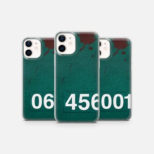 Peut inclure: Trois coques de téléphone transparentes avec un design vert et blanc. Les coques présentent un numéro "06 456001" imprimé au dos. Les coques ont des éclaboussures de peinture brunes au dos.