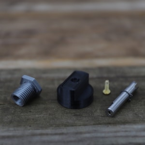 Puede incluir: Un conjunto de cuatro piezas metálicas de color plateado para un objeto impreso en 3D. Las piezas incluyen un tornillo pequeño, una varilla larga, una perilla pequeña y una perilla más grande.