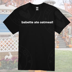 May include: Black t-shirt with white text that reads "babette ate oatmeal!" The shirt is a unisex style and has a crew neck.