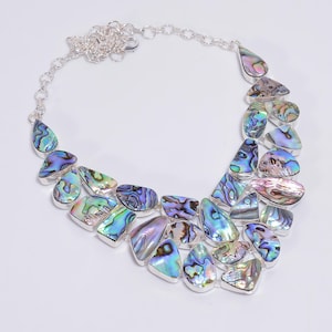 May include: A silver necklace featuring a large, iridescent abalone shell pendant. The pendant is composed of numerous smaller, irregularly shaped pieces of abalone shell, each displaying a distinctive pattern of colours.