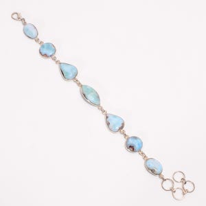 Peut inclure: Un bracelet en argent orné de pierres de larimar bleu clair de formes variées, ovales, en goutte et rondes. Les pierres ont des inclusions brunes et sont reliées par des maillons en argent. Le bracelet est présenté sur fond blanc. Mesure environ 18 cm.