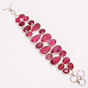 May include: A silver bracelet with a row of pink ruby gemstones. The bracelet has a lobster clasp closure.