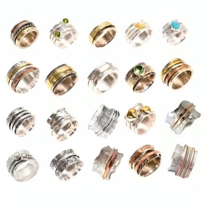 Può includere: Una collezione di anelli spinner argentati con vari design. Alcuni anelli presentano accenti dorati, ramati e di pietre preziose, tra cui turchese e peridoto. Gli anelli presentano motivi e texture intricati, mostrando una varietà di stili e abbellimenti.