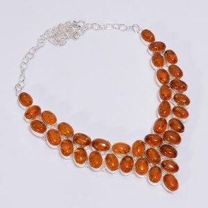 Könnte beinhalten: Eine silberne Halskette mit mehreren ovalen Bernsteinsteinen. Die Bernsteinsteine haben eine warme, durchscheinende orange-braune Farbe und sind in einzelnen Silberfassungen gefasst. Die Halskette hat ein Doppelstrang-Design.