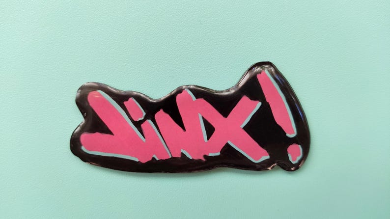 May include: A black and pink sticker with the word "Lixx!" written in a stylized font.