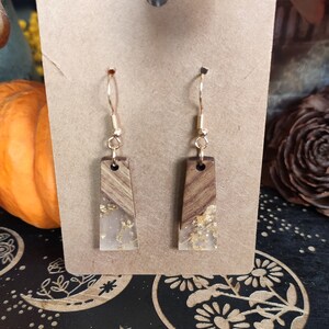 May include: A pair of gold dangle earrings with rectangular wood and clear resin accents. The resin has gold flakes embedded in it.