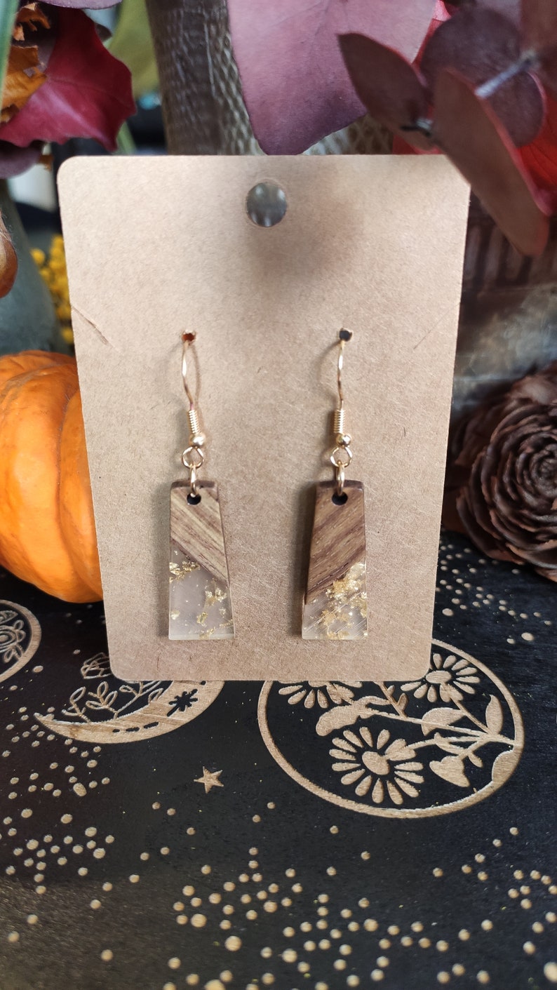 May include: A pair of gold dangle earrings with rectangular wood and clear resin accents. The resin has gold flakes embedded in it.