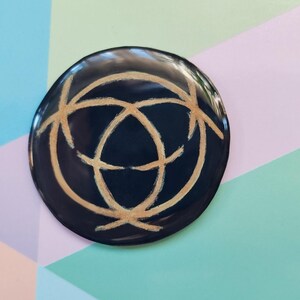 May include: A black circular coaster with a gold geometric design. The coaster has a smooth, glossy finish.