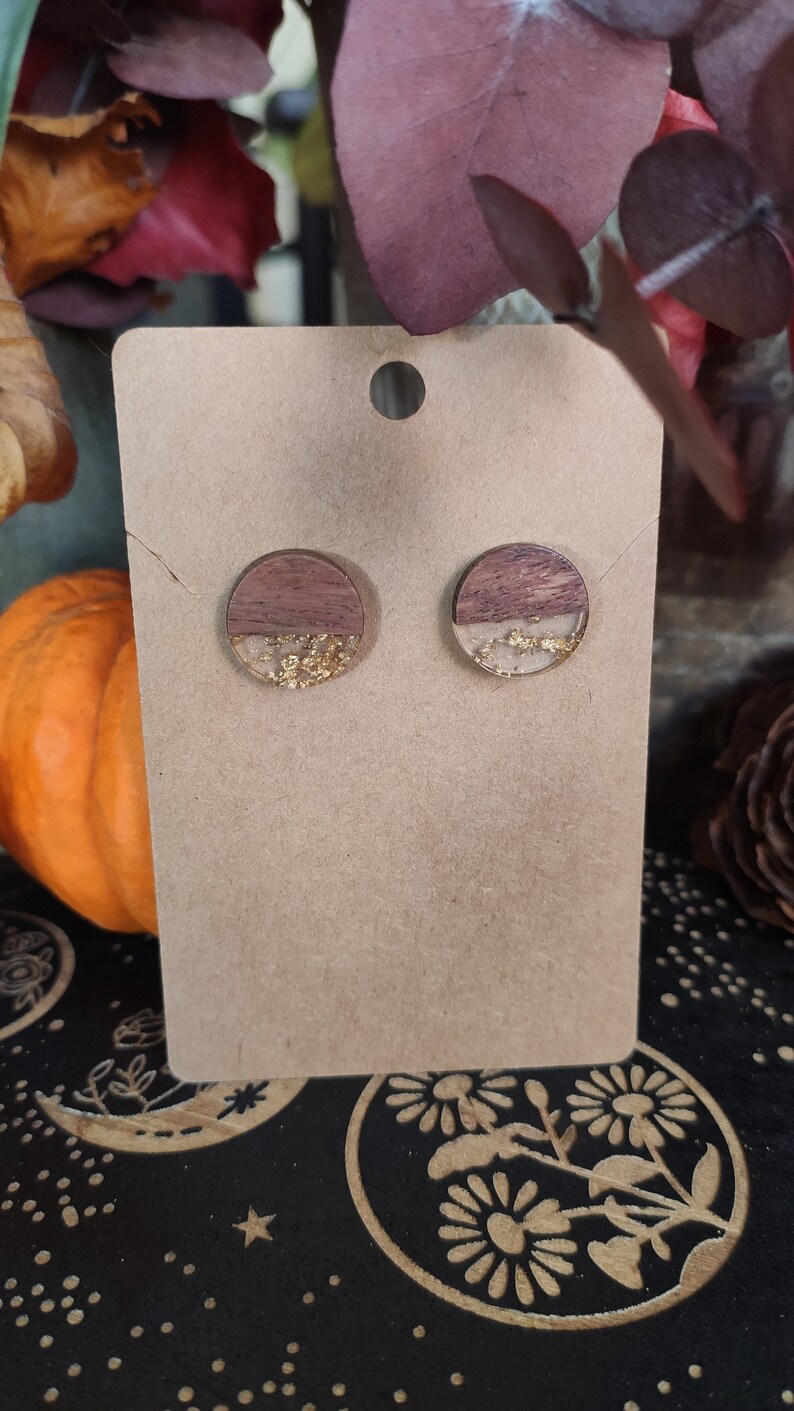 May include: A pair of round wooden earrings with a brown and white wood grain pattern and gold glitter embedded in clear resin.