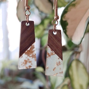 May include: A pair of gold dangle earrings with a clear resin and wood design. The resin is filled with gold flakes.