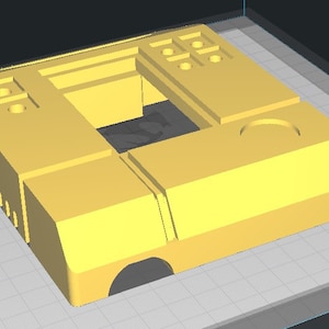 May include: A yellow plastic 3D printed model of a rectangular box with a square opening in the center. The box has several small holes and a larger circular hole on the top.