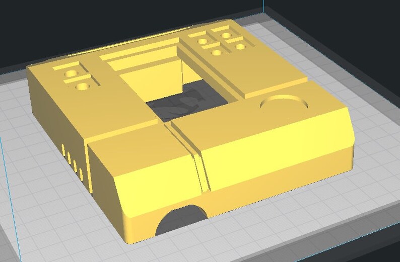 May include: A yellow plastic 3D printed model of a rectangular box with a square opening in the center. The box has several small holes and a larger circular hole on the top.