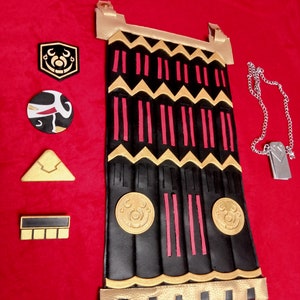 May include: A black leather pouch with gold trim and red accents. The pouch has a decorative design of zigzags and vertical lines. There are four circular gold accents on the front of the pouch. The pouch is surrounded by five small decorative pieces, including a gold triangle, a black and white circle, a black and gold circle, and two black rectangles.