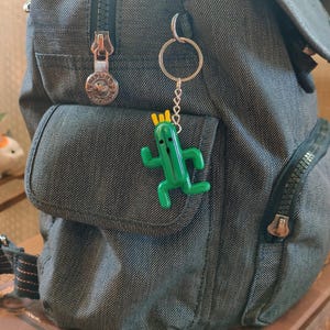 May include: A dark gray backpack with a zippered pocket and a green cactus keychain. The keychain is attached to a silver key ring with a silver chain.