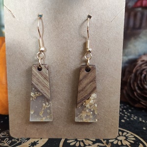 May include: A pair of gold dangle earrings with a clear resin and wood design. The resin is filled with gold flakes.