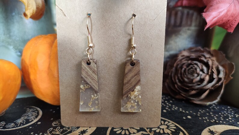 May include: A pair of gold dangle earrings with a clear resin and wood design. The resin is filled with gold flakes.