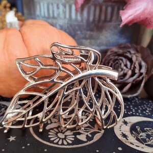 May include: Gold leaf-shaped hair clip with a delicate, intricate design. The clip is made of metal and has a spring-loaded mechanism for holding hair in place.