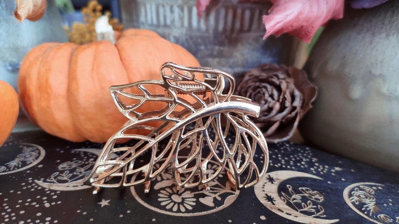 May include: Gold leaf-shaped hair clip with a delicate, intricate design. The clip is made of metal and has a spring-loaded mechanism for holding hair in place.