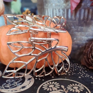 May include: Gold leaf-shaped hair clip with a delicate, intricate design. The clip is resting on a small orange pumpkin.
