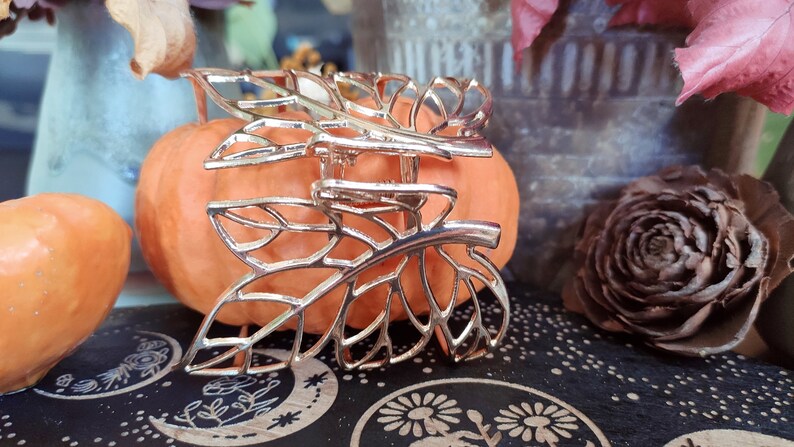 May include: Gold leaf-shaped hair clip with a delicate, intricate design. The clip is resting on a small orange pumpkin.