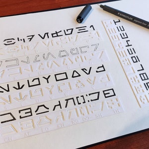 May include: A white notebook with black lines and symbols. The notebook is open and has a black pen on top of it. The symbols are in a variety of shapes and sizes. The text on the pen reads "STABILO Pigment Liner 0.3".