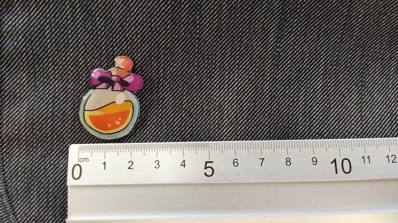 May include: A small, round, clear glass bottle with a pink bow and orange liquid inside. The bottle is about 2 cm in diameter.