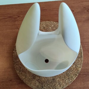 May include: White ceramic planter shaped like a rabbit's head with a drainage hole at the bottom. The planter is sitting on a cork coaster.