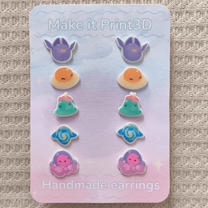 May include: A set of handmade earrings on a pastel gradient card. The earrings feature various colorful designs, including purple winged creatures, orange suns, teal plants, blue swirls, and pink octopuses. The card reads "Make it Print3D" and "Handmade earrings."