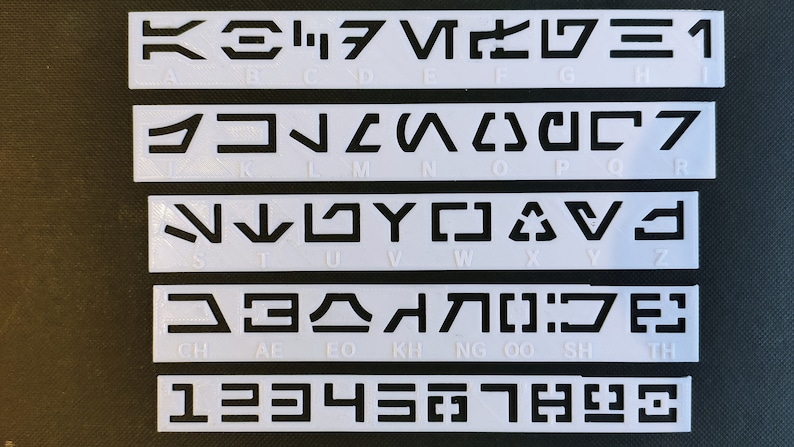 Peut inclure: Pochoirs en plastique blanc avec des symboles noirs pour l'alphabet et les chiffres. Les symboles sont pour l'alphabet Aurebesh, un alphabet fictif utilis&eacute; dans l'univers Star Wars. Les pochoirs sont dispos&eacute;s en rang&eacute;es, chaque rang&eacute;e contenant un ensemble diff&eacute;rent de symboles. La premi&egrave;re rang&eacute;e contient les lettres A &agrave; H, la deuxi&egrave;me rang&eacute;e contient les lettres I &agrave; R, la troisi&egrave;me rang&eacute;e contient les lettres S &agrave; Z, la quatri&egrave;me rang&eacute;e contient les lettres CH, AL, EO, KH, NG, OO, SH et TH, et la cinqui&egrave;me rang&eacute;e contient les chiffres 1 &agrave; 9.