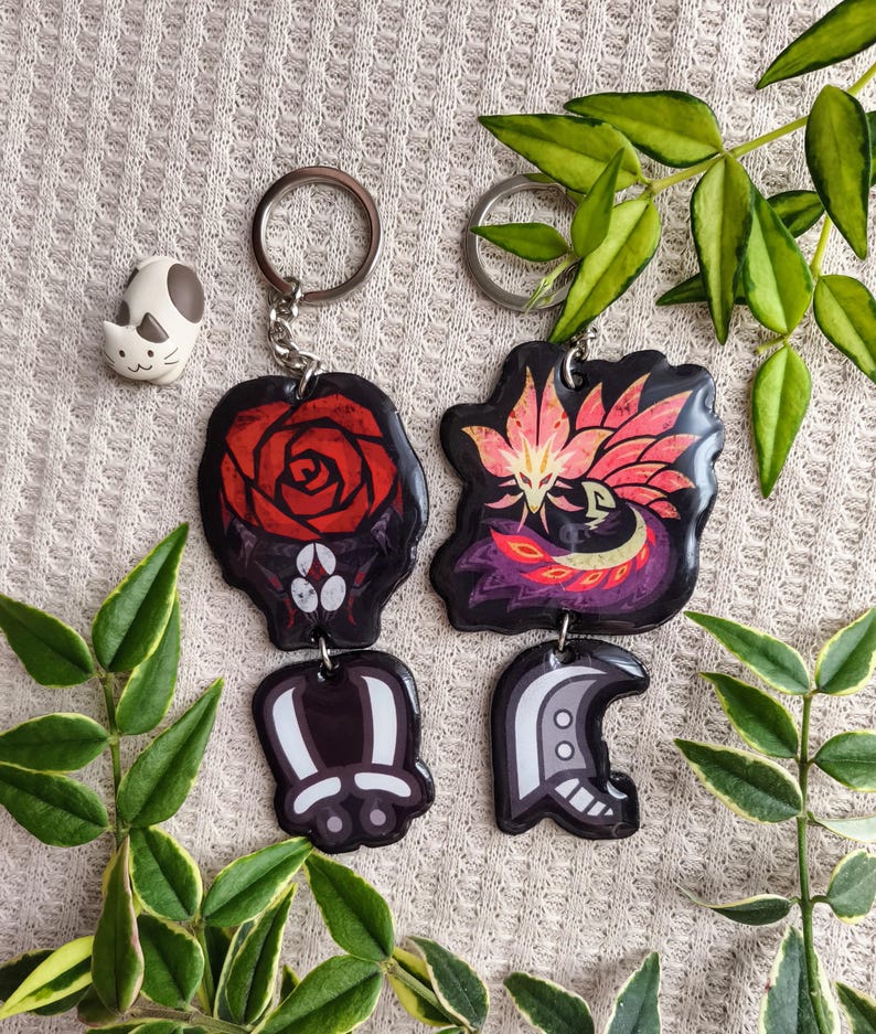 May include: Keychains with unique designs. One keychain features a red rose, another a stylized bird with pink and orange feathers. Two additional keychains have abstract shapes. A small cat figurine is also present.