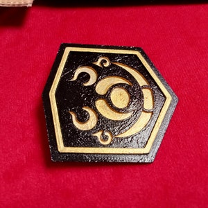 May include: A black hexagonal wooden coaster with a gold design of a crescent moon and stars. The coaster has a textured surface.