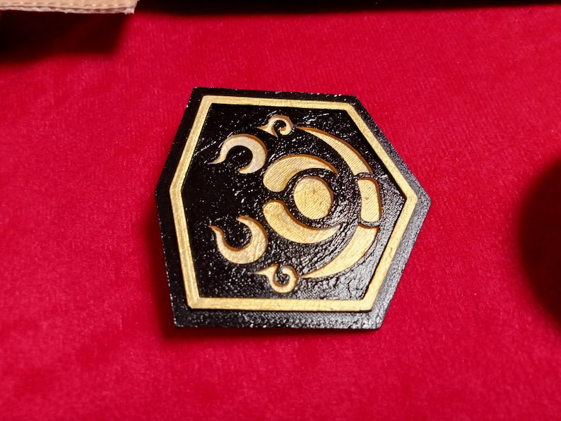 May include: A black hexagonal wooden coaster with a gold design of a crescent moon and stars. The coaster has a textured surface.