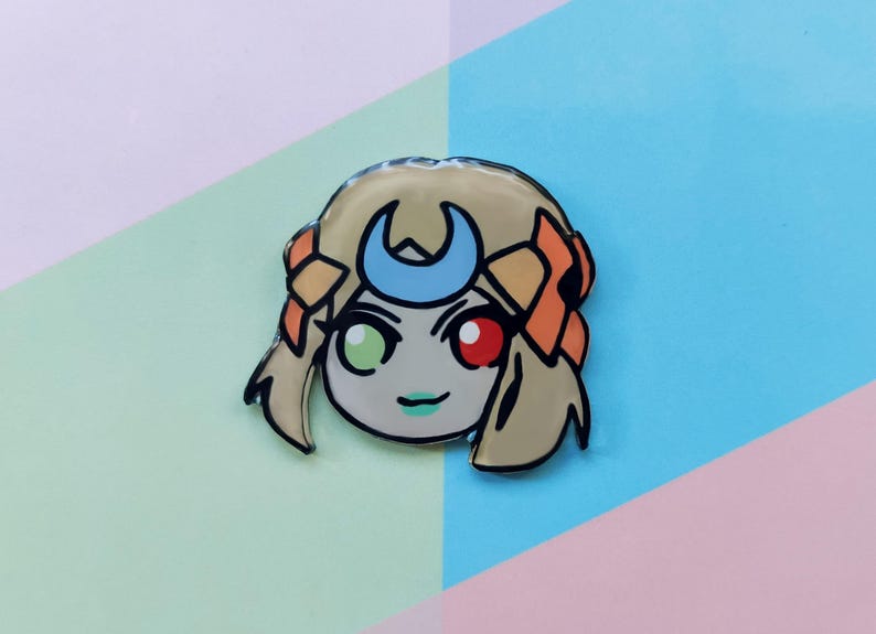 May include: A cartoon character with blonde hair, a crescent moon headband, and green and red eyes. The character is wearing a light brown outfit and has a light green background.