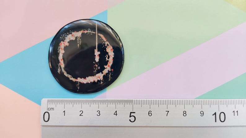 May include: A black and white button with a red and white design. The button is 5 cm in diameter.