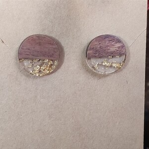 May include: A pair of round wood and resin earrings with gold flakes. The earrings are a light brown colour with a clear resin top half and gold flakes embedded in the resin.