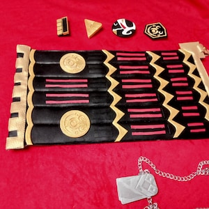 May include: A black and gold decorative belt with red stripes and circular designs. A silver dog tag with a chain is also pictured.