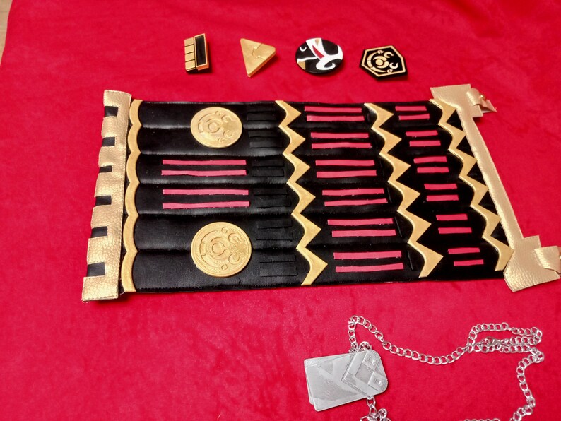 May include: A black and gold decorative belt with red stripes and circular designs. A silver dog tag with a chain is also pictured.