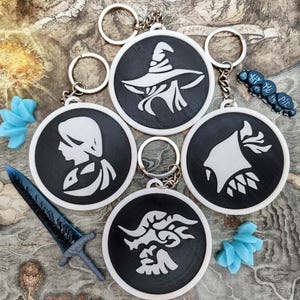 May include: A collection of black and white keychains with various fantasy-themed designs, including a wizard, a profile, and a creature. The keychains are round and have silver key rings. Also included are a blue sword and blue decorative flowers.