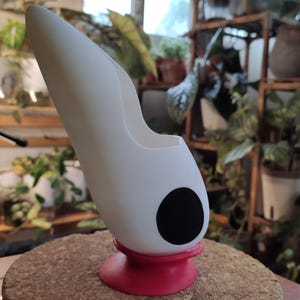 May include: White ceramic planter with a black circle design and a red base. The planter is shaped like a curved, elongated vase.