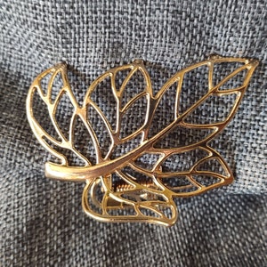 May include: Gold-toned metal hair clip shaped like a leaf with a delicate, intricate design.