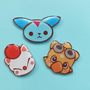 May include: Three colorful cartoon character pins. The first pin is blue with a pink nose and white eyes. The second pin is white with a red hat and pink eyes. The third pin is yellow with a brown beak and gray goggles.