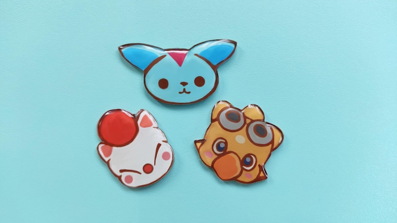 May include: Three colorful cartoon character pins. The first pin is blue with a pink nose and white eyes. The second pin is white with a red hat and pink eyes. The third pin is yellow with a brown beak and gray goggles.