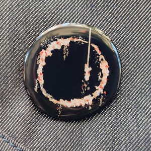May include: A black and white button with a red and white circle design. The circle has a white line through it.