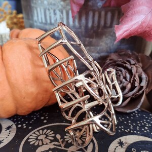 May include: A gold metal hair claw with a delicate, intricate design resembling a leaf or branch. The claw is open and ready to hold hair.