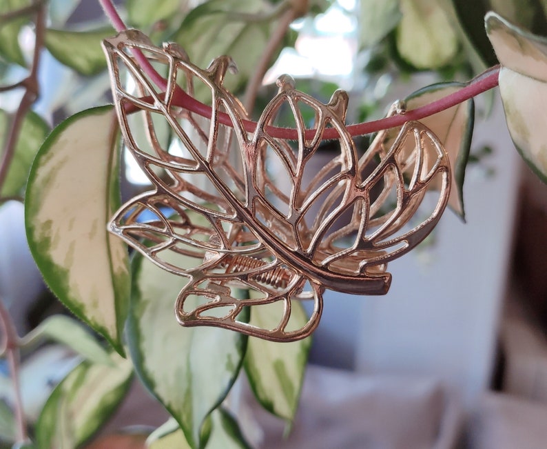May include: A gold leaf-shaped hair clip with a delicate, intricate design. The clip is made of metal and has a spring-loaded mechanism.
