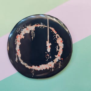 May include: A black button with a red and white circle design. The circle is a stylized power button symbol.